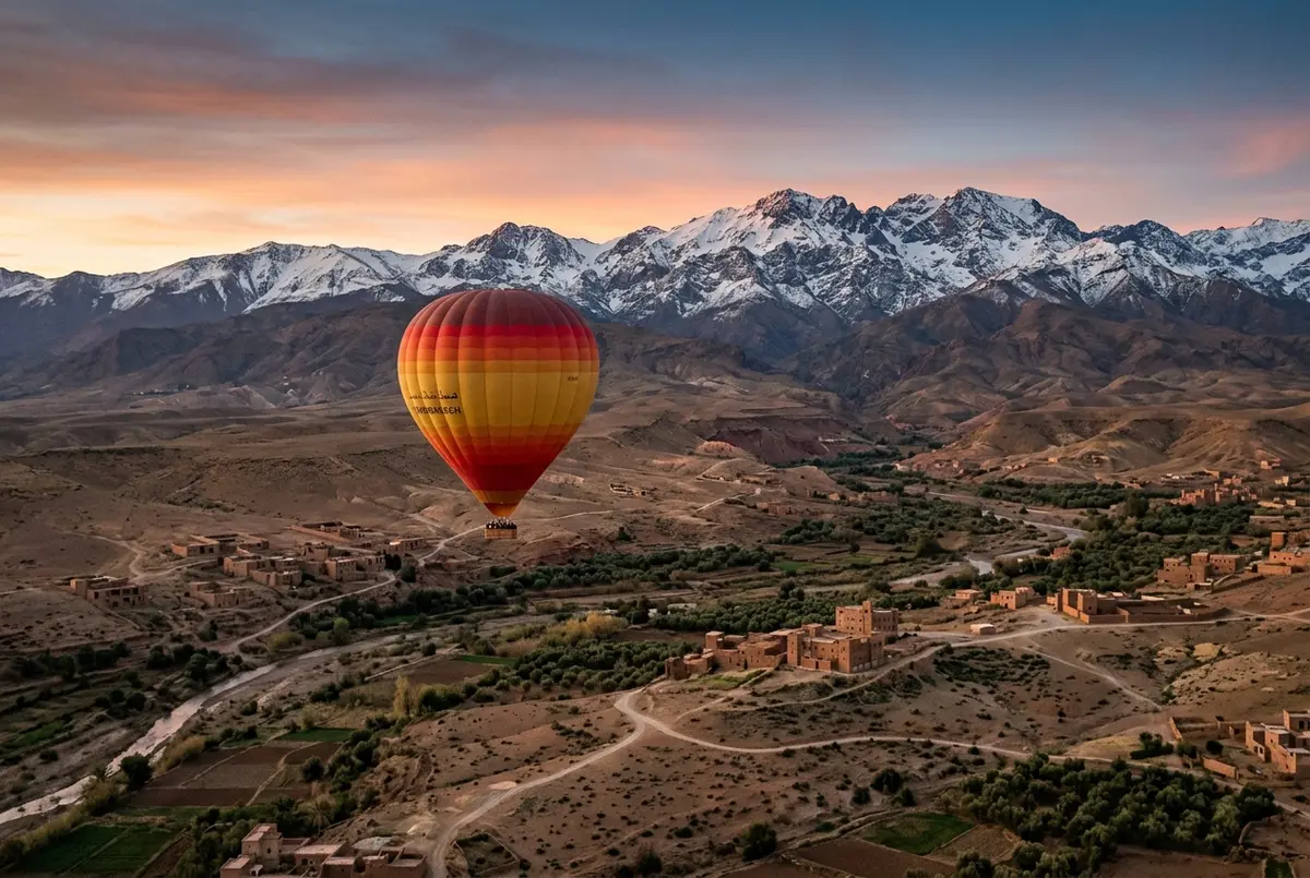 Hot air balloon drifting above the Marrakech countryside with the snow capped High Atlas Mountains rising sharply on the horizon at sunrise, atlas mountains hot air balloon scene